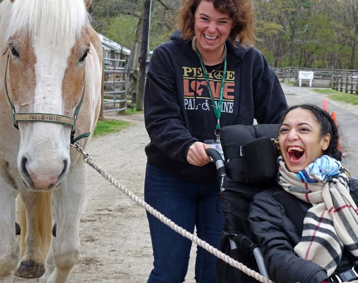 WOMAN BEING PUSHED IN WHEEL CHAIR WHILE HOLDING A HORSE'S LEAD
